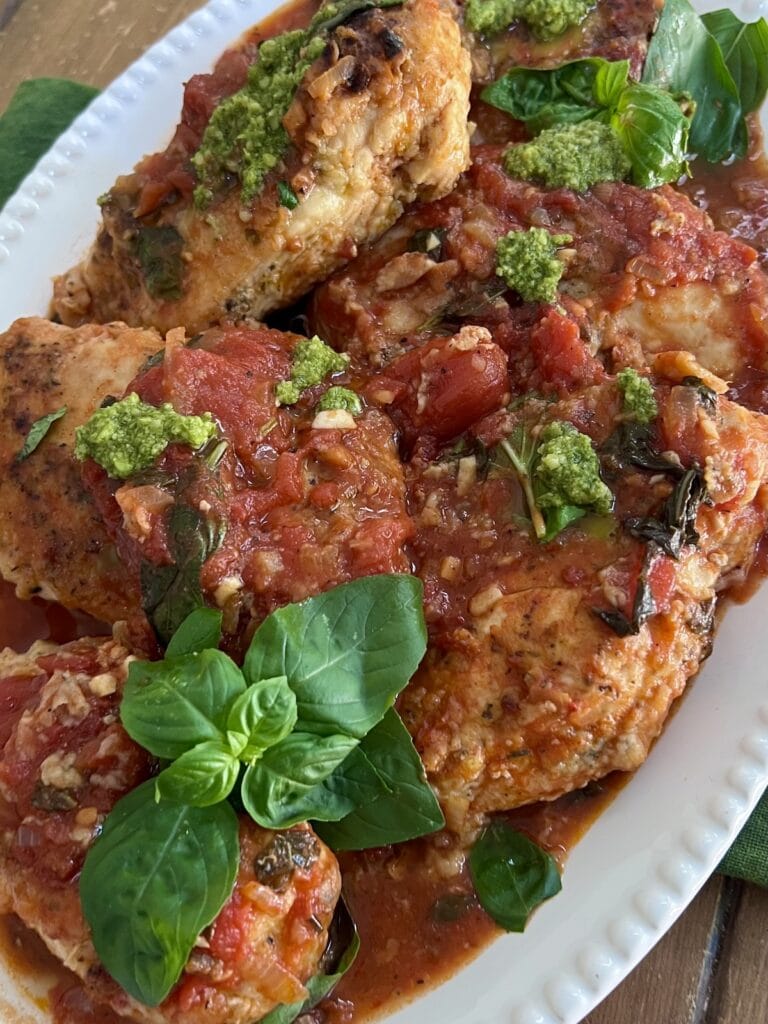 Platter of chicken pomodoro with basil and pesto garnish.