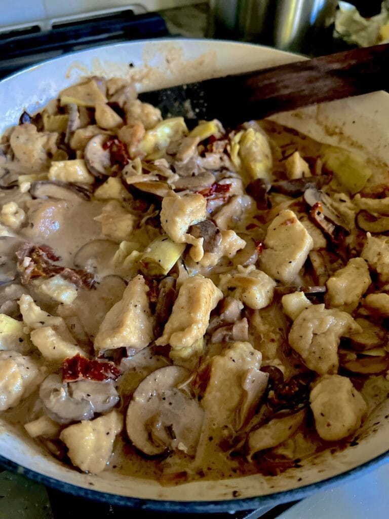 Stirring cooked chicken pieces back into sauce in pan.