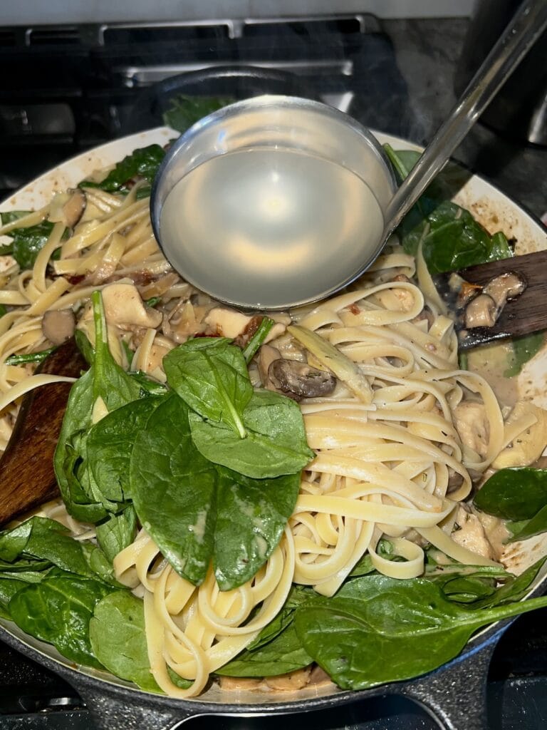 Adding pasta water to pasta and sauce with stainless steel ladle.