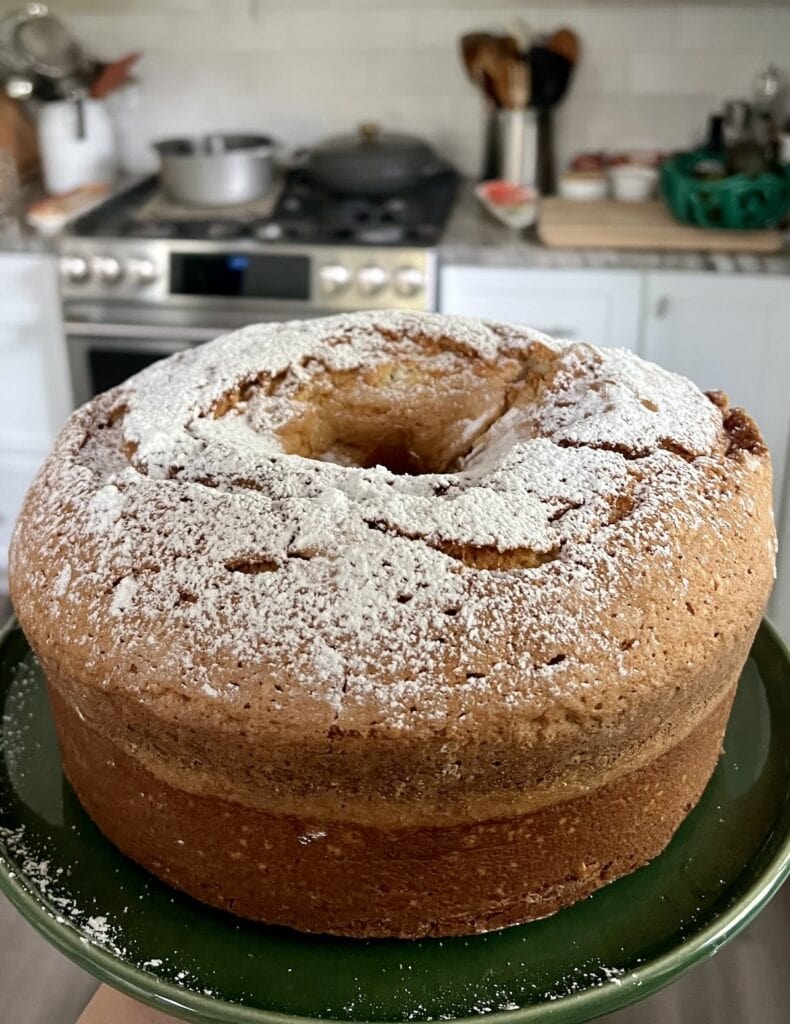 Old fashioned sour cream pound cake on green plate with kitchen in the background.