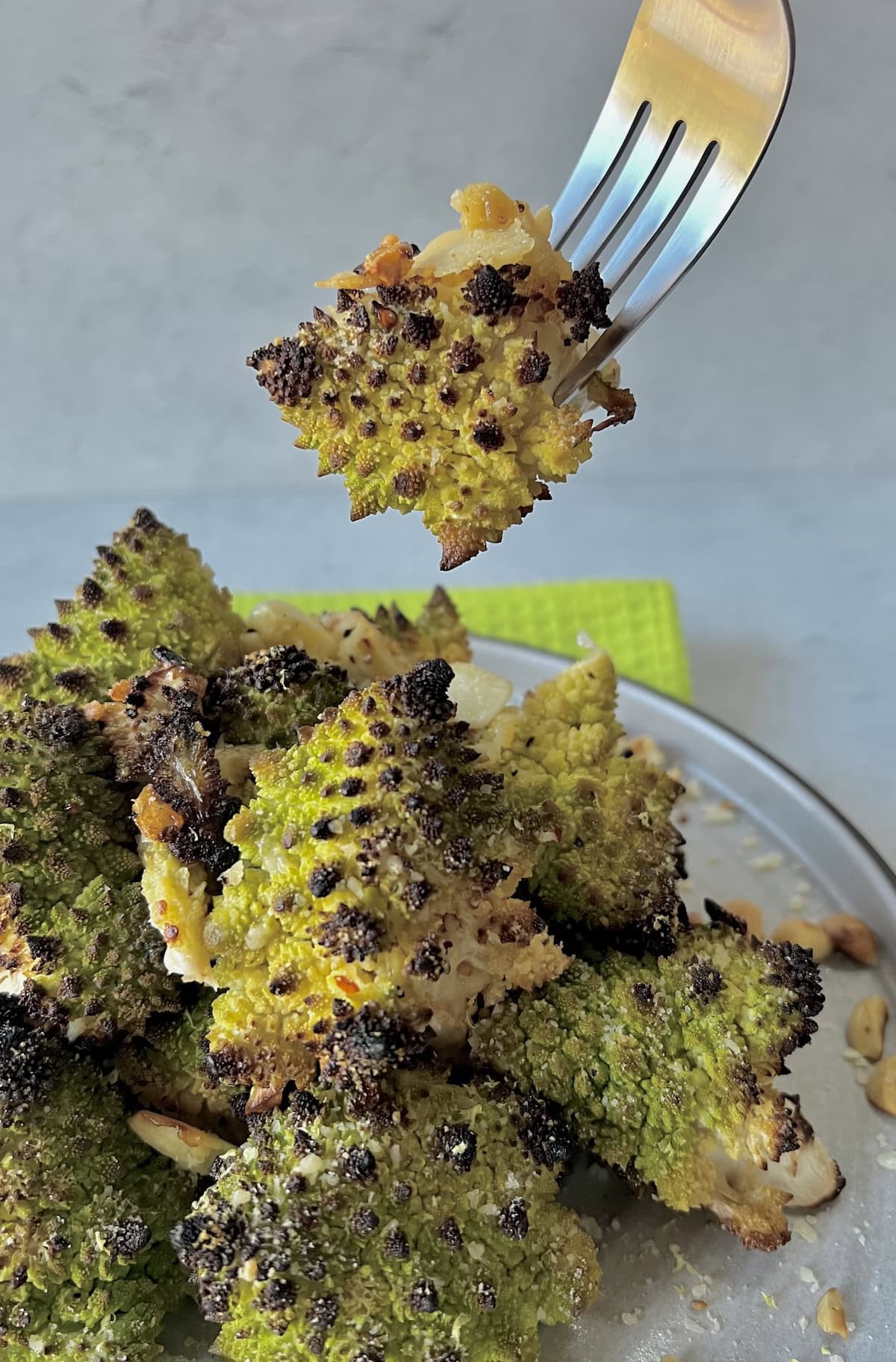 Close up of a piece of roasted Romanesco cauliflower on fork over a plate of it.