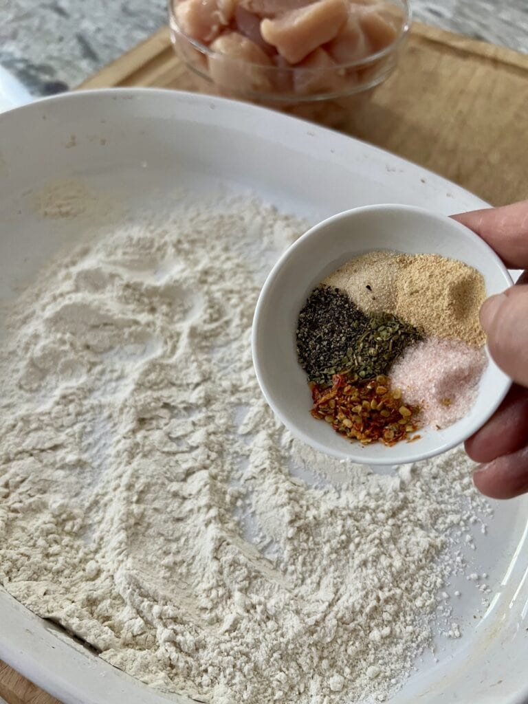 Adding spices to flour to be used to coat chicken.