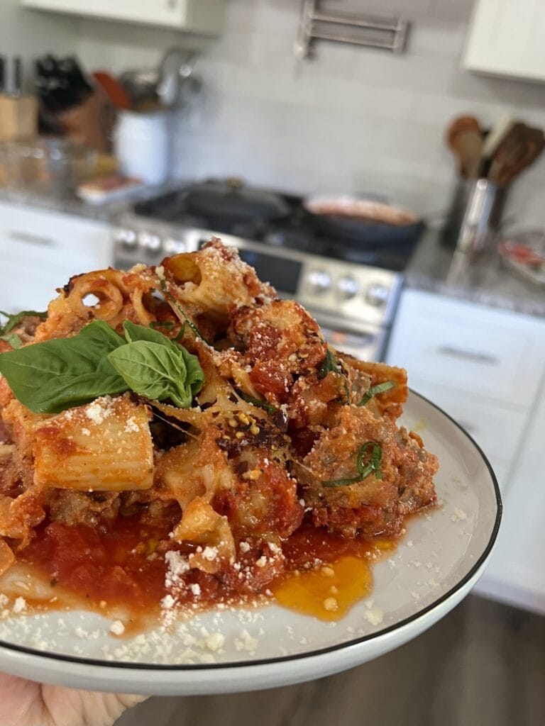Close up of rigatoni al forno with basil leaves and kitchen in the background.