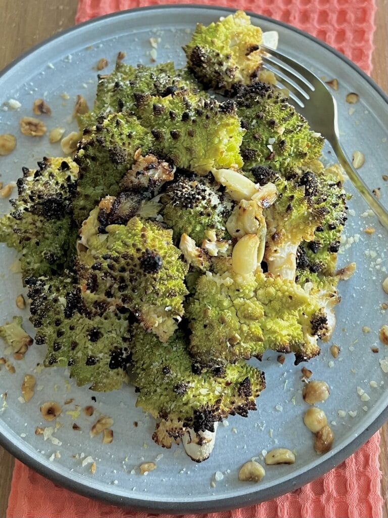 Lemon Roasted Romanesco Broccoli on plate with toasted hazelnuts and fork, over decorative towel.
