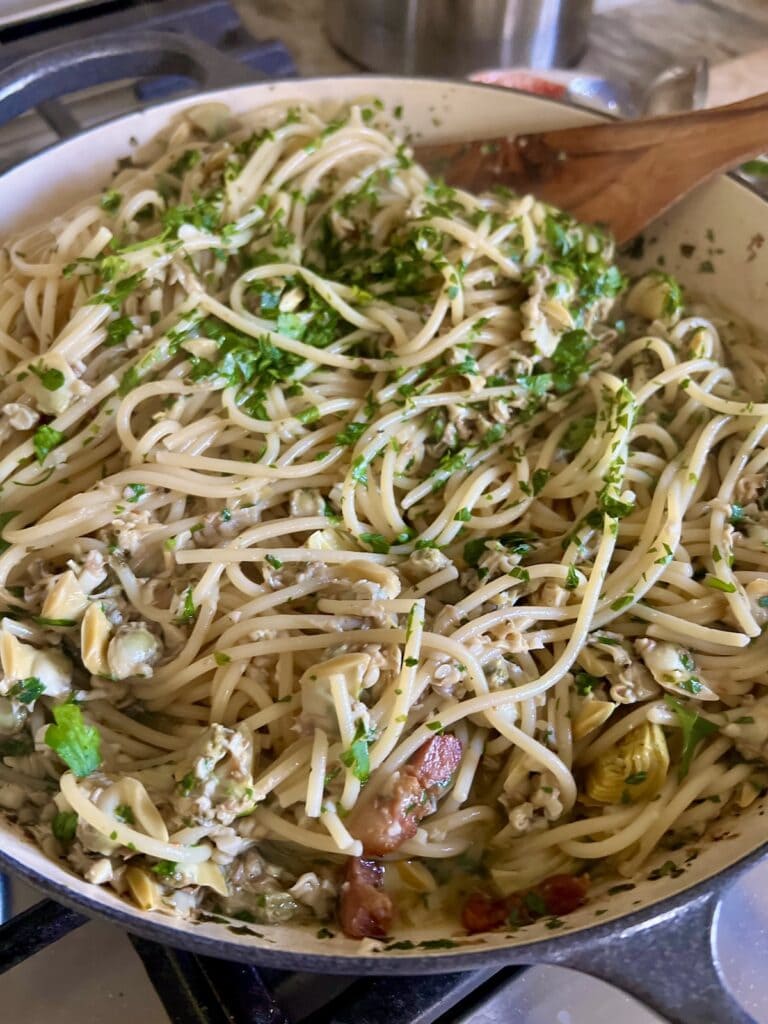 Mixing all pasta with canned clams ingredients together in pan.