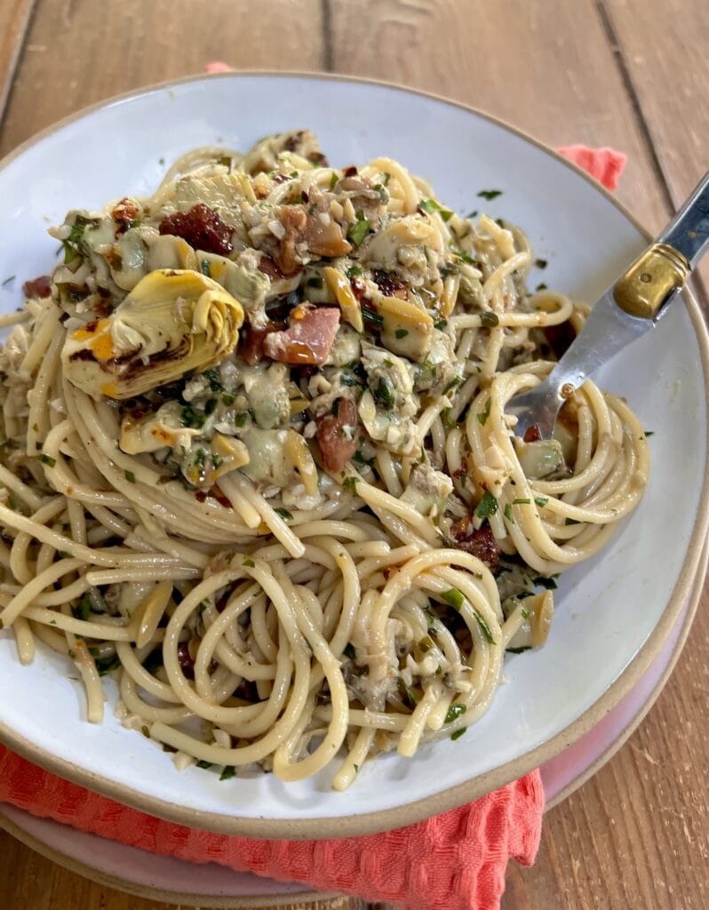 Spaghetti with Canned Clams in white pasta bowl with fork over decorative towel.