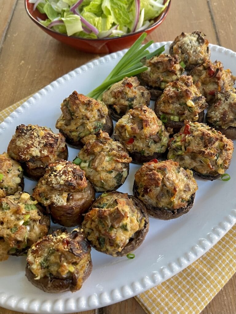 Chicken Marsala Stuffed Mushrooms on white serving platter with green onion garnish and green salad in background.