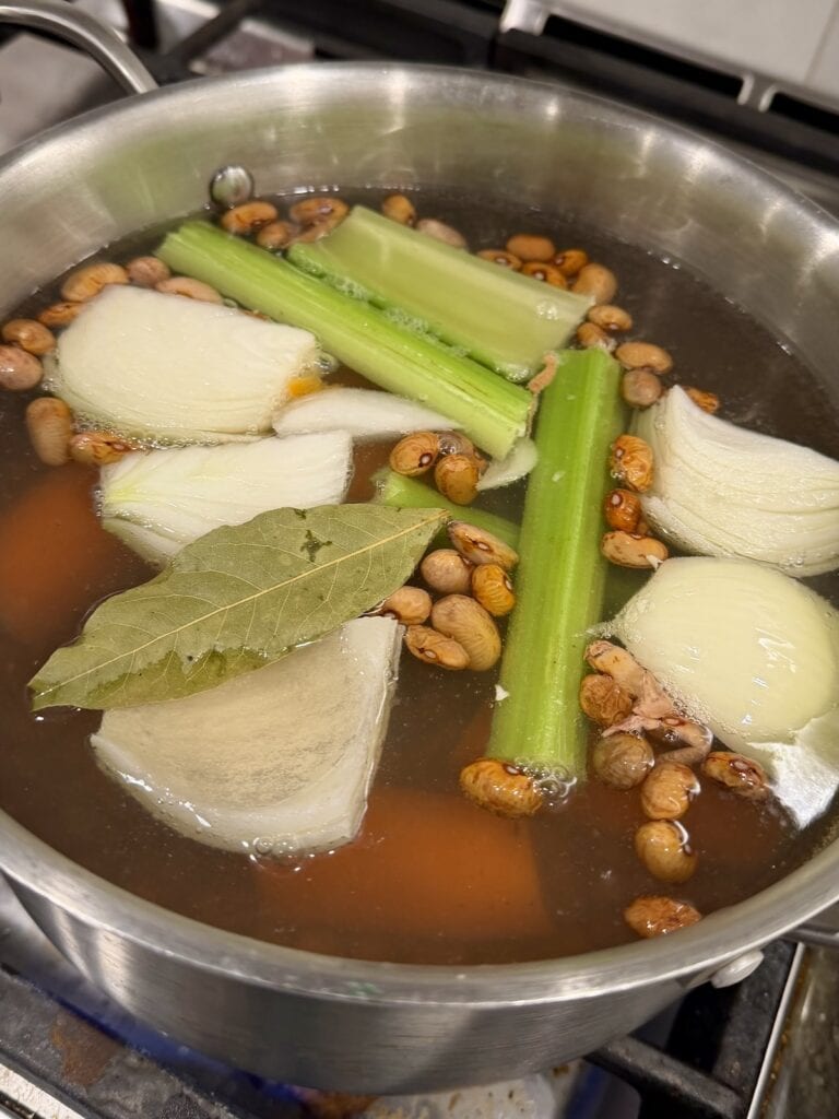 Cooking beans with aromatics in pot of boiling water.
