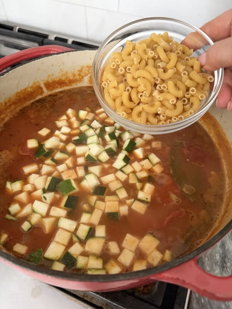 Adding pasta elbows to pot of soup.