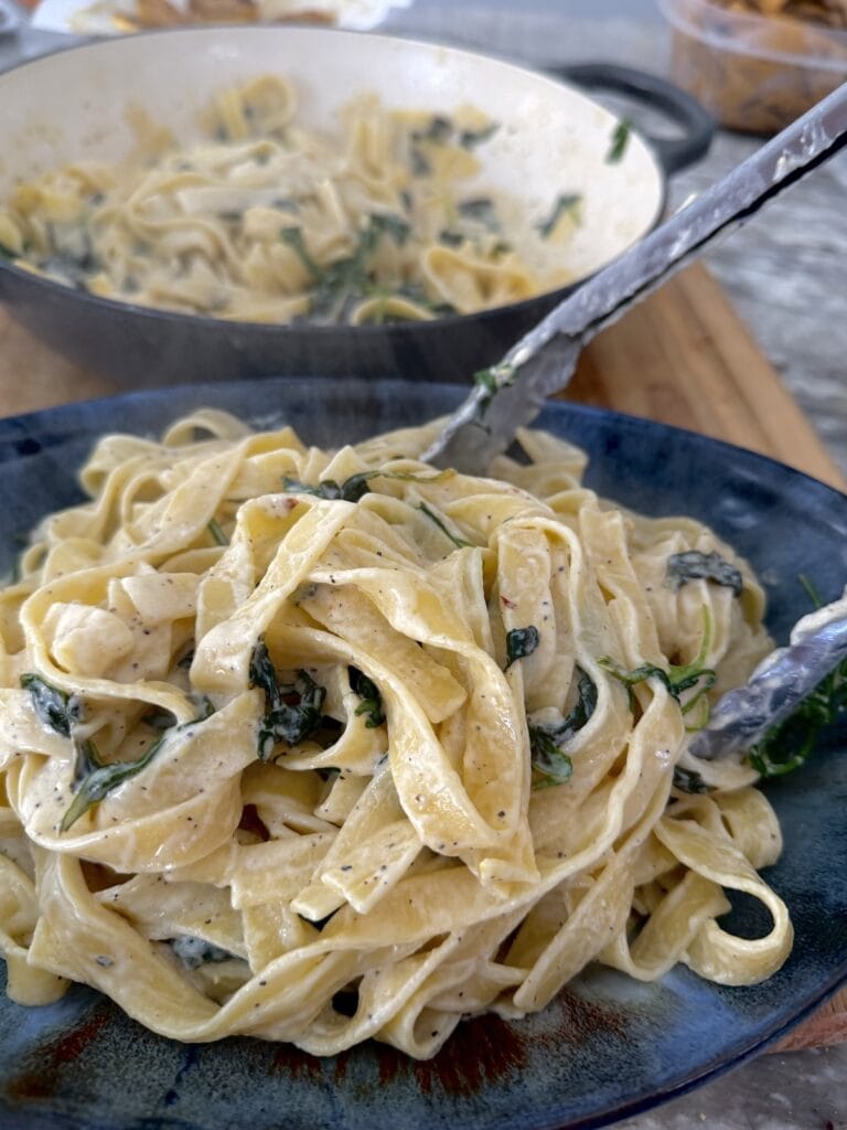 Transferring Tagliatelle al Limone from pot to blue serving platter with tongs.