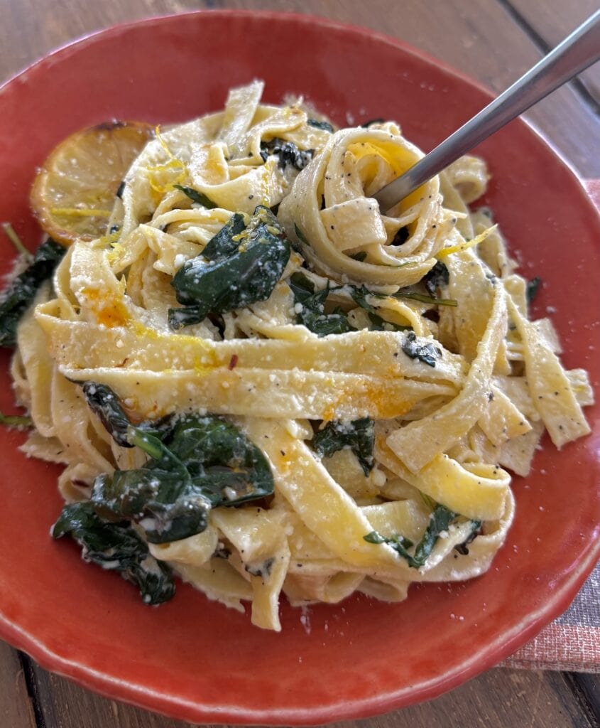 Twirling some creamy lemon tagliatelle on a fork in an orange pasta bowl.