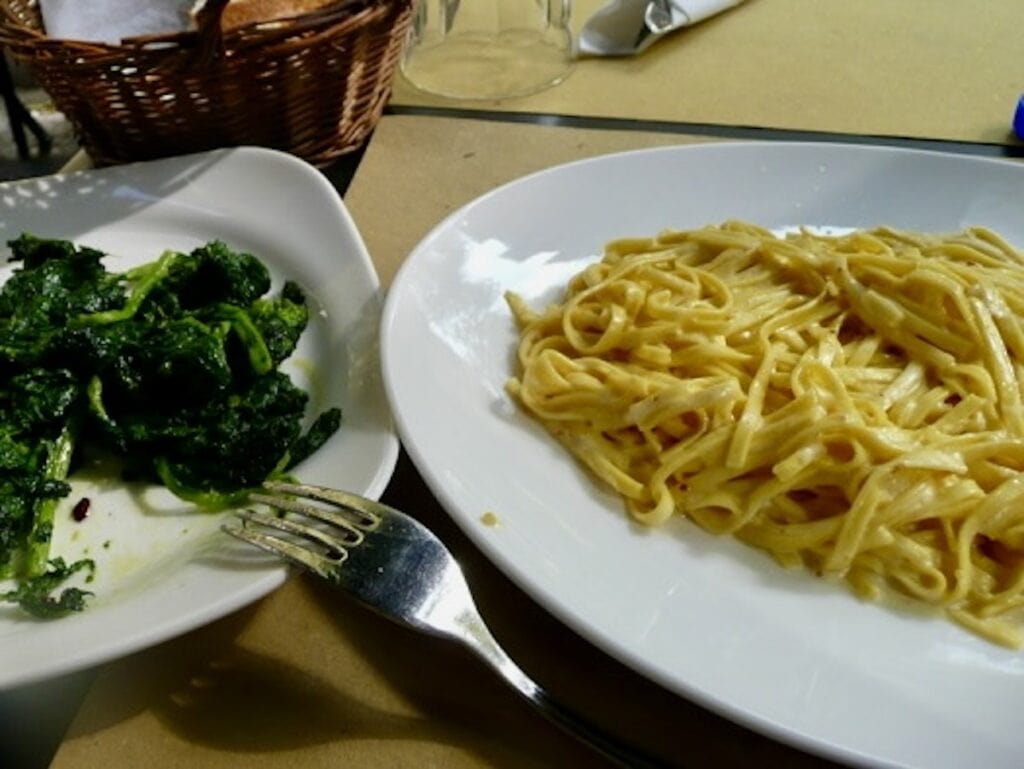 Plates of pasta al limone and saut&eacute;ed spinach at a restaurant in Rome.