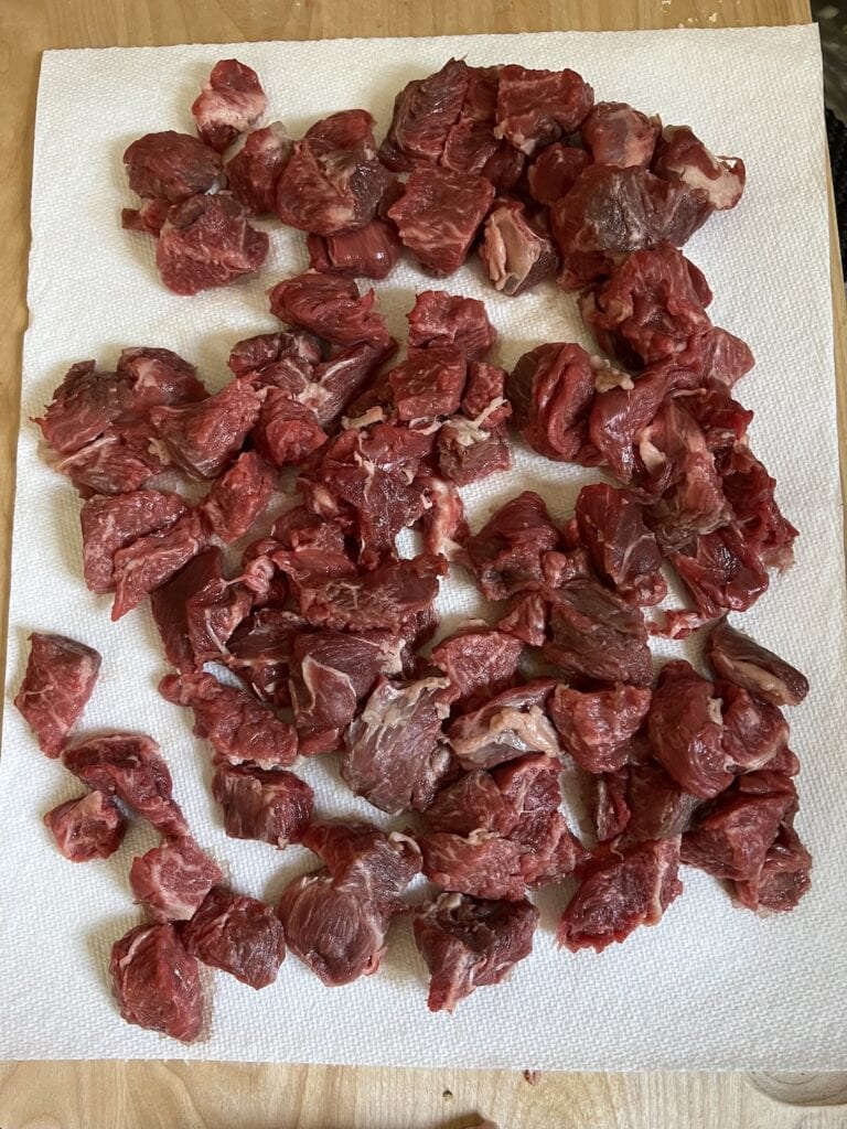 Bite-sized pieces of chuck roast patted dry and ready to coat with flour for Italian beef soup.