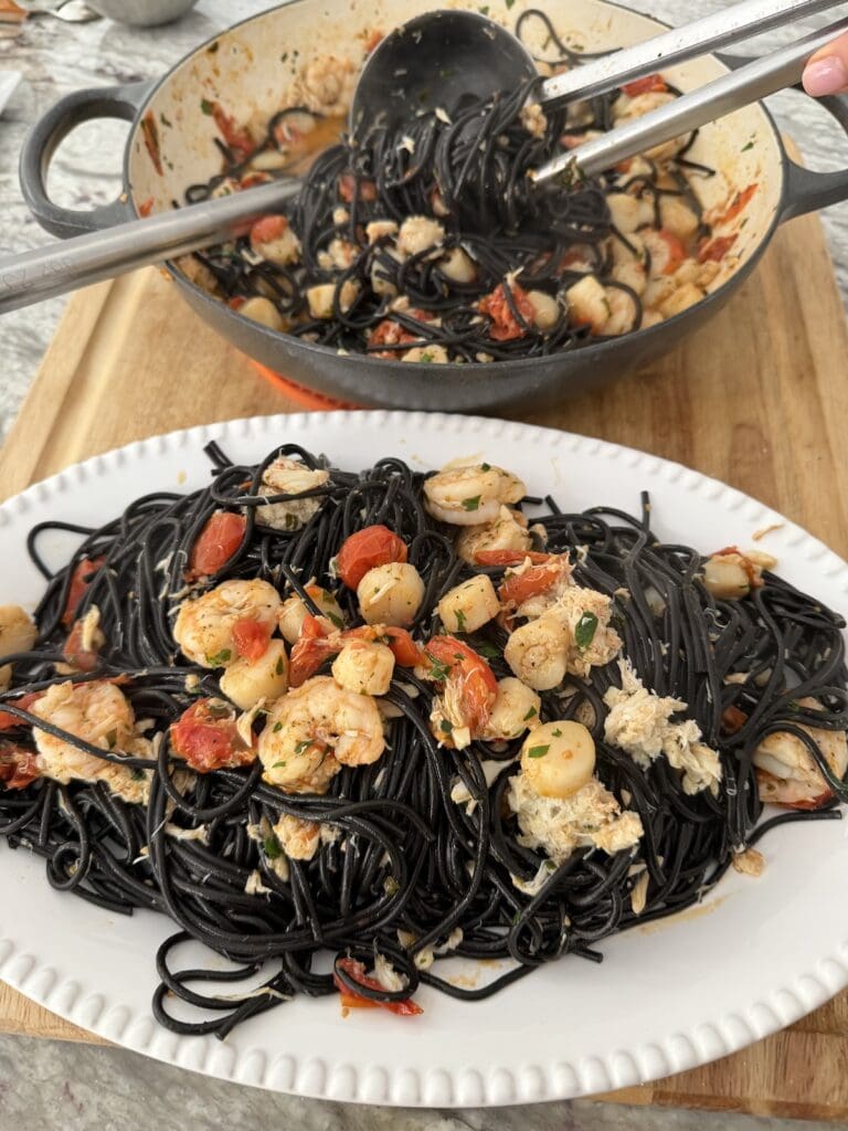 Pasta with Mixed Seafood in white serving platter with more Squid Ink Seafood Pasta in the background.