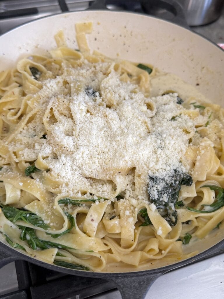 Grated cheese just added to pasta al limone in pan.
