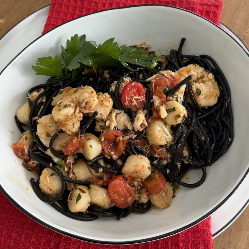 Squid Ink spaghetti with mixed seafood in white dinner bowl.