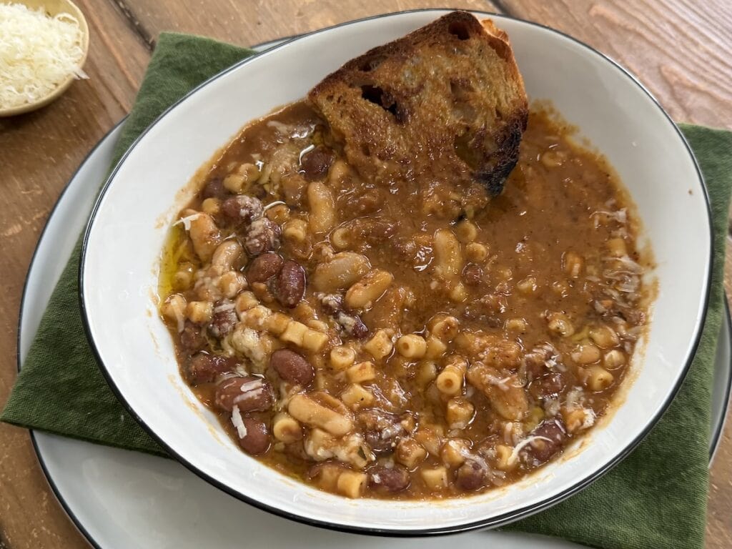 Creamy Pasta Fagioli Soup with toasted bread in white soup bowl over decorative towel.