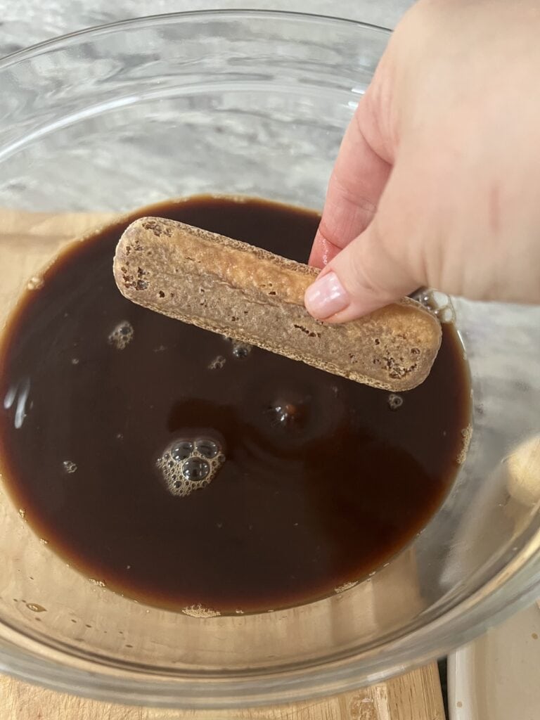 Dipping a ladyfinger cookie into coffee mixture.