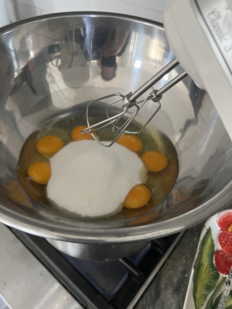 Hand mixer in bowl with eggs and sugar.
