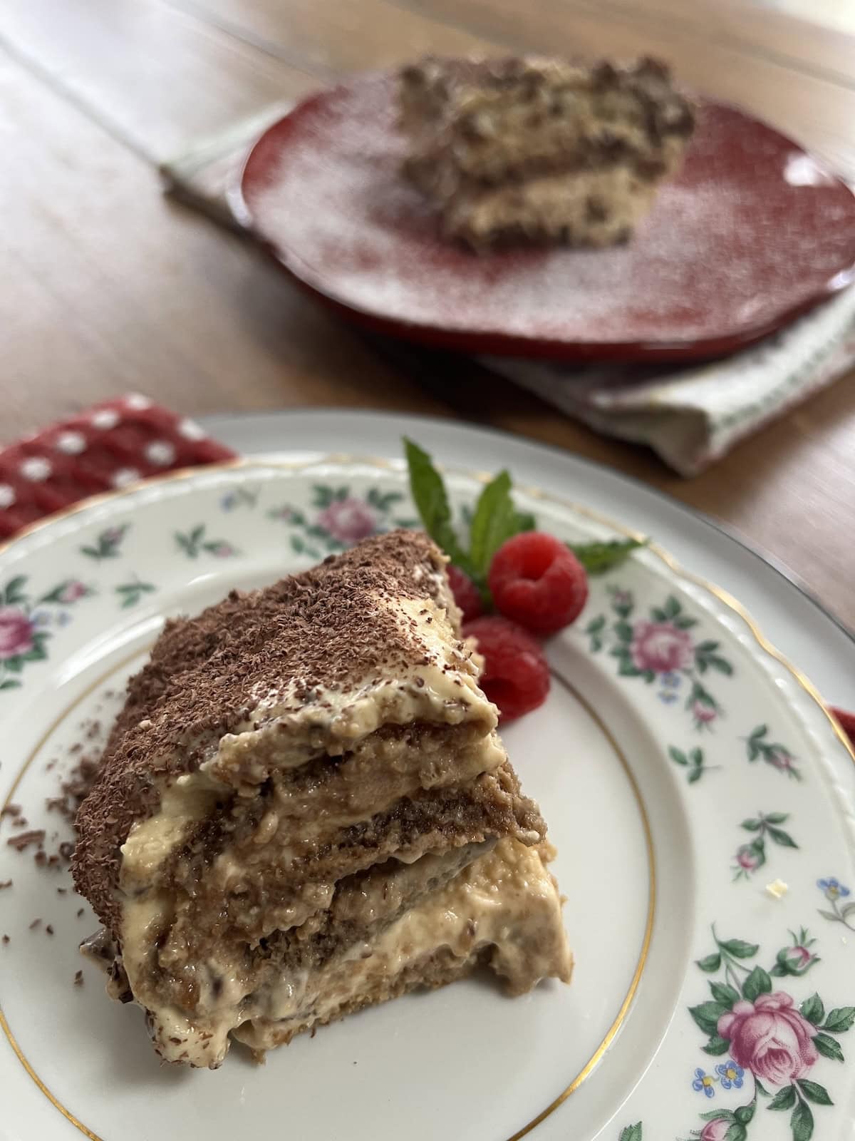 Slice of Tiramisu Classico on china plate with another slice on a red plate in the background.