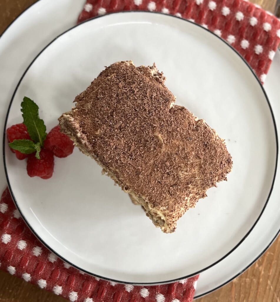 Overhead view of a slice of Authentic Italian Tiramisu  on white dessert plate with raspberry garnish.