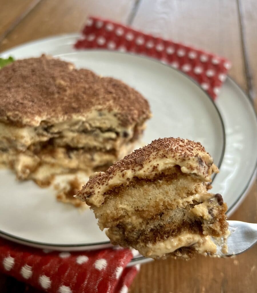 Up close view of a piece of Classic Italian Tiramisu Recipe on fork, with rest of slice in the background.