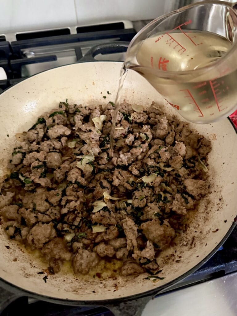 Pouring wine into sauce to deglaze.