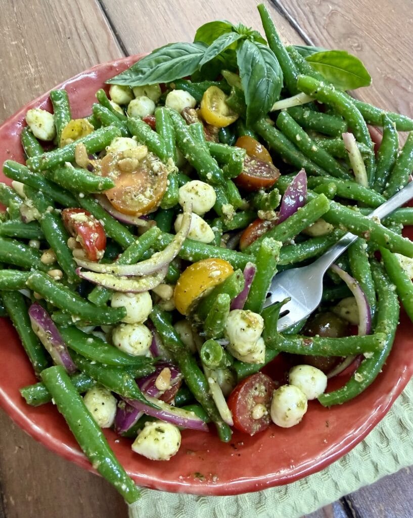 Italian string bean salad in orange bowl with basil garnish and fork.