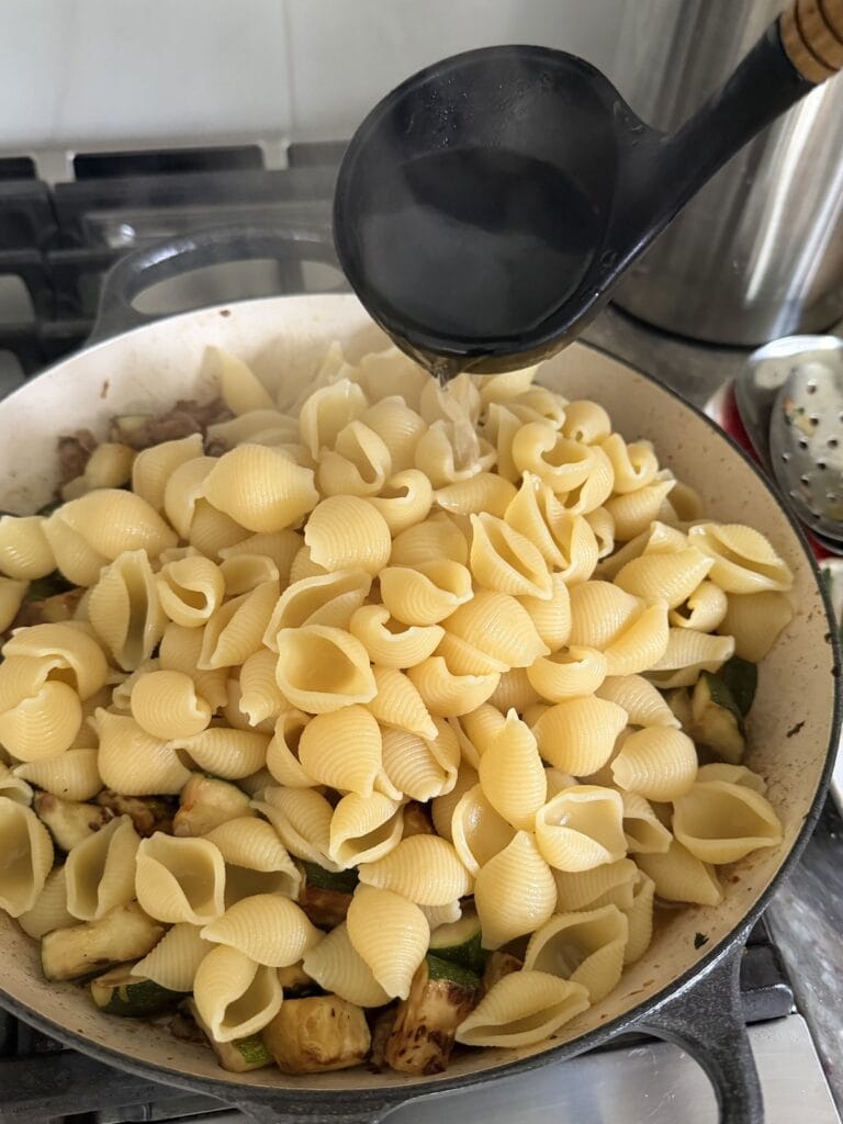 Pouring a ladelful of pasta water into the pasta and sauce.