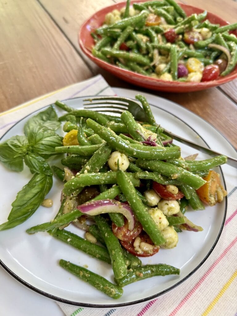 Pesto green bean salad on white dish with fork and bowl of it in the background.