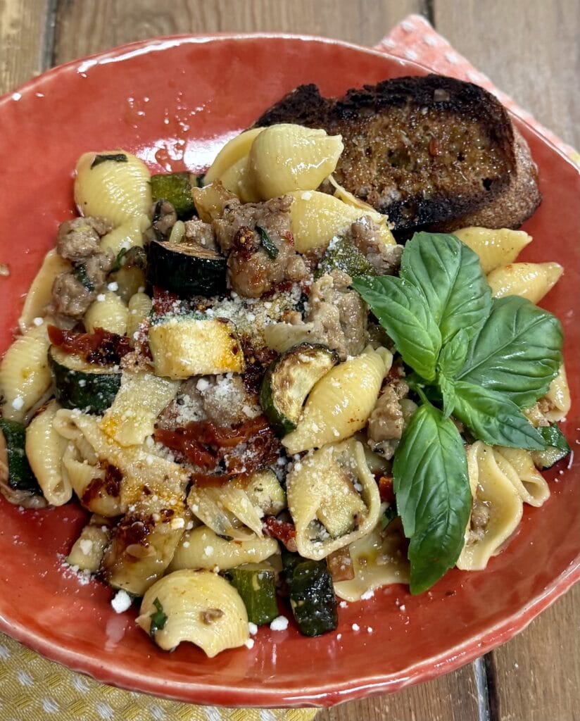 Pasta with Sausage and Zucchini  in orange pasta bowl with basil garnish and bread.