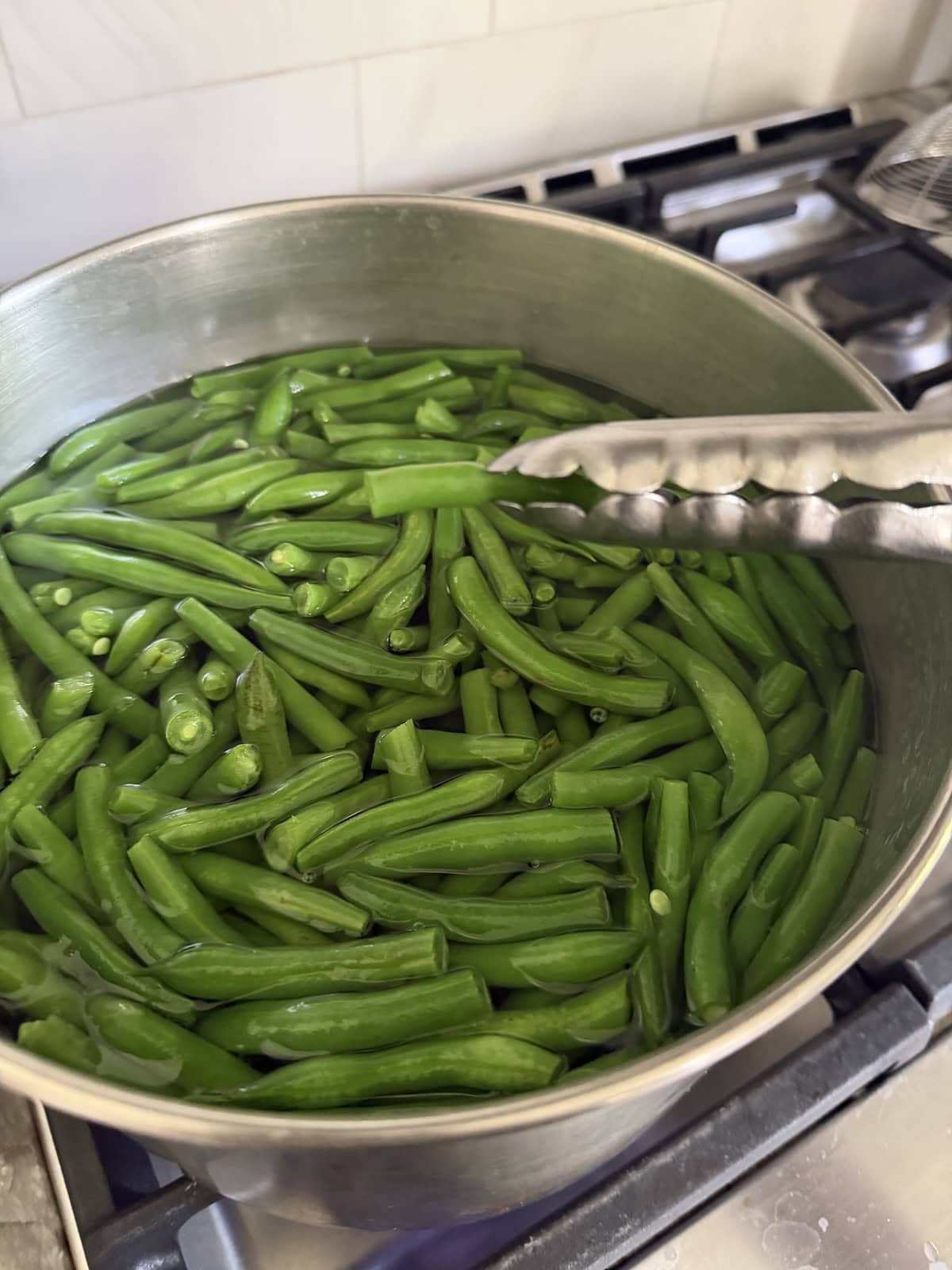 Testing out the tenderness of green bean with tongs.