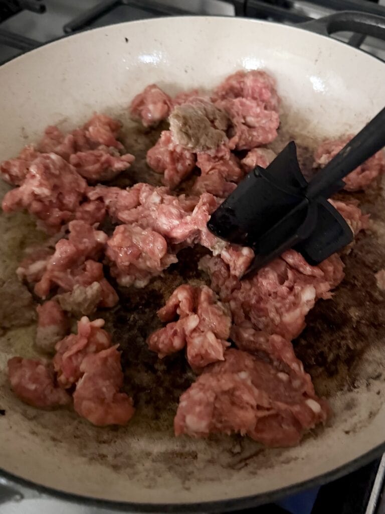 Browning sausage in pan and breaking it up with utensil into bite-sized pieces.