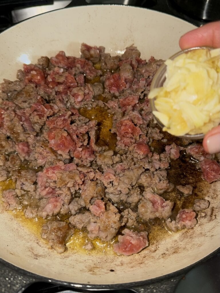 Adding garlic to sausage for Easy Zucchini and Sausage Pasta.