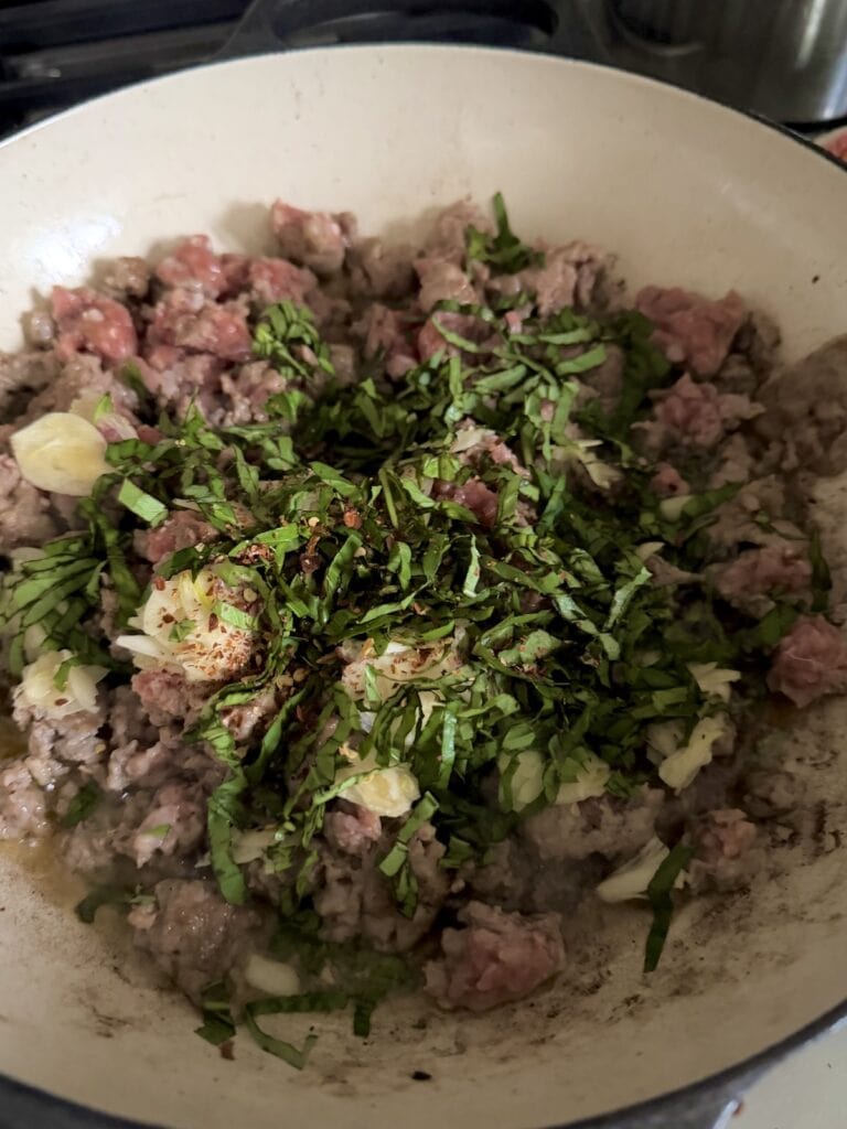 Basil, garlic and crushed red pepper flakes added to sausage in pan.