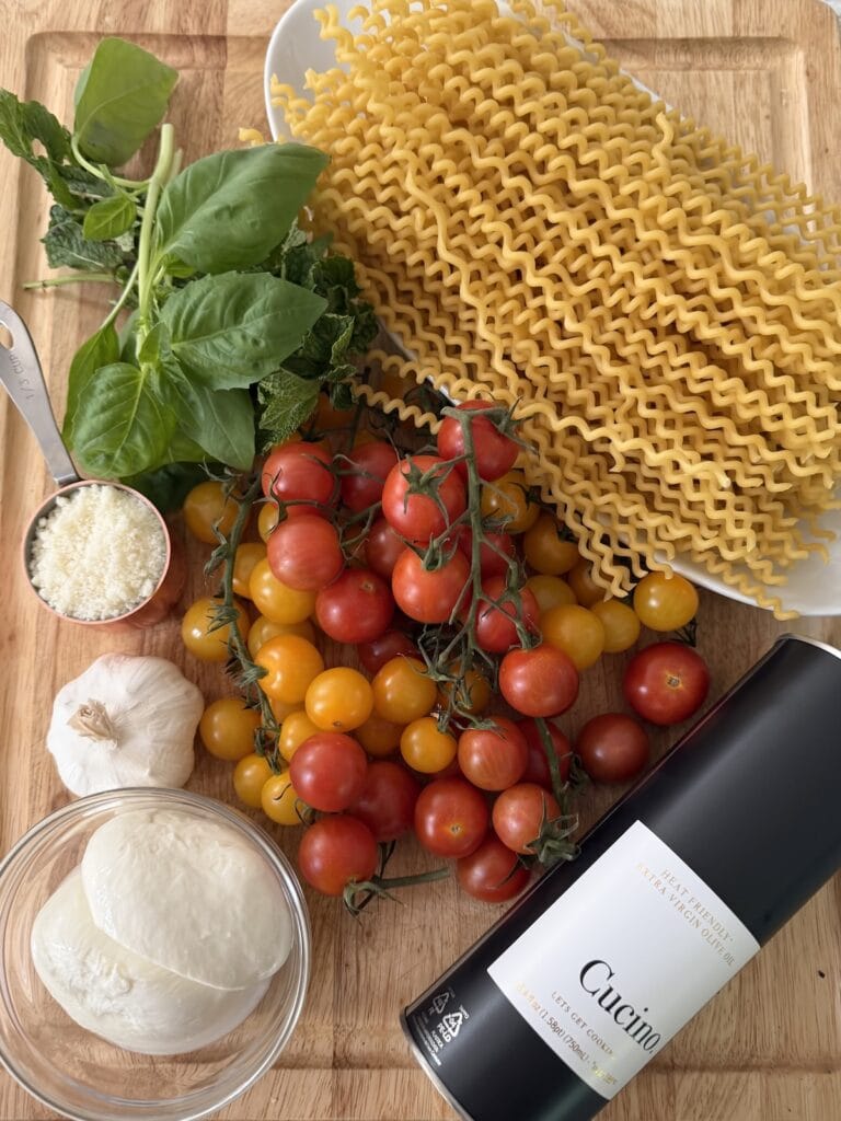 All ingredients for Easy Summer Pasta Recipe with burrata and burst cherry tomatoes on cutting board.