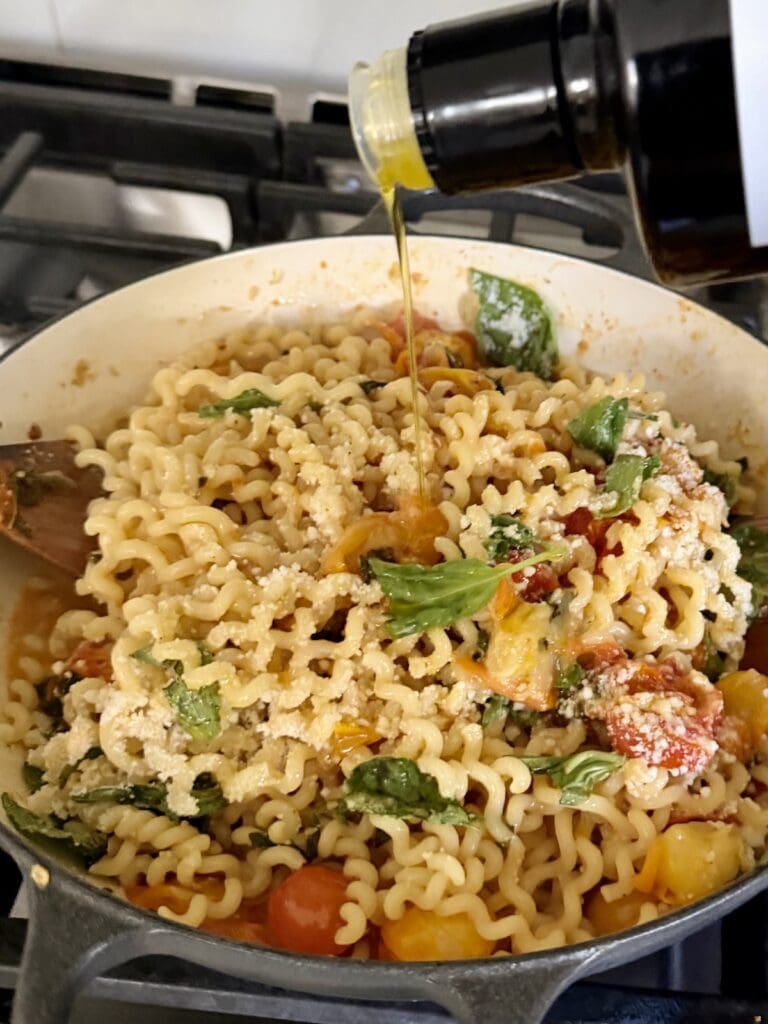 Drizzling some extra virgin olive oil over finished cherry tomato pasta.