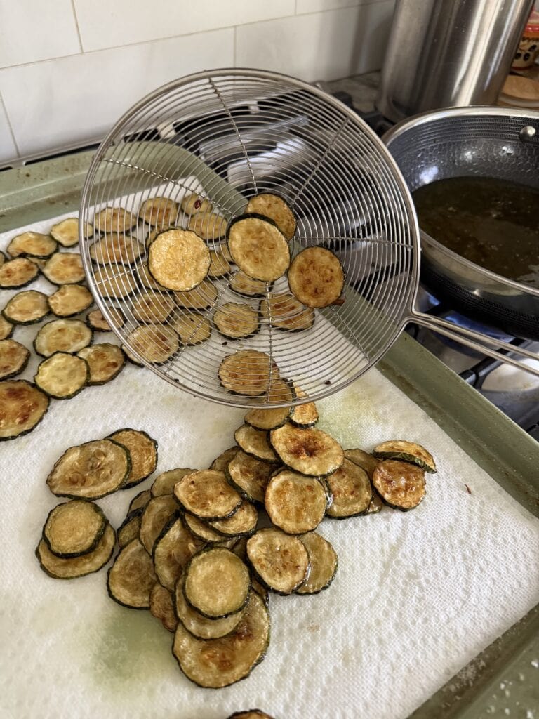 Placing fried zucchini on paper towel-line sheet pan.