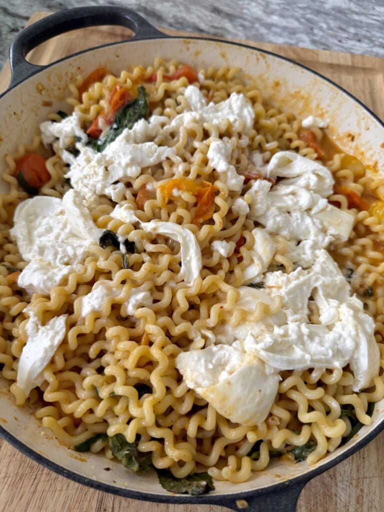 Burrata cheese spread out over burst cherry tomato pasta.