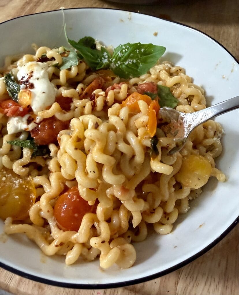 Close up of some burst cherry tomato pasta on fork, with basil garnish.