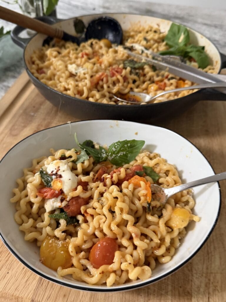 Blistered Cherry Tomato Pasta with burrata in pasta bowl with fork and pot of pasta behind it.