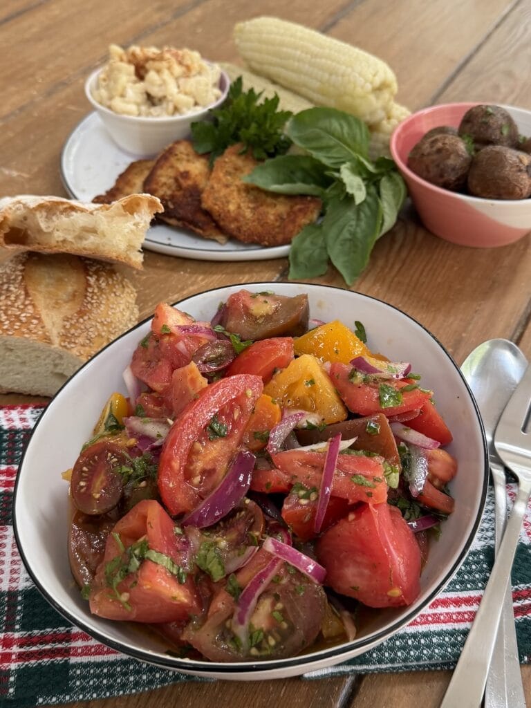 A large bowl of Italian marinated tomatoes surrounded by other dinner items, including bread.