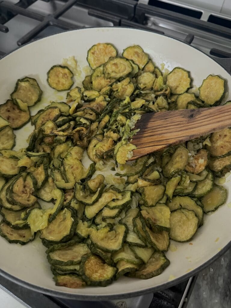 Mixing up and breaking up the fried zucchini in pan to a chunky mixture with wooden spoons.