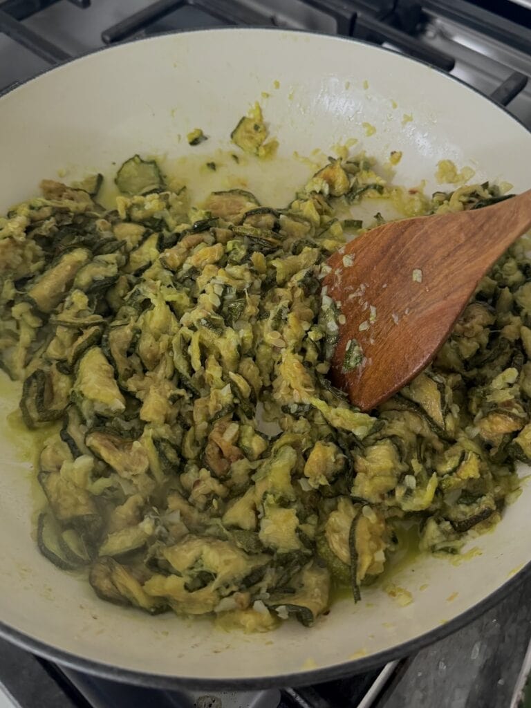 Mixing up and breaking up the fried zucchini in pan to a chunky mixture with wooden spoons.