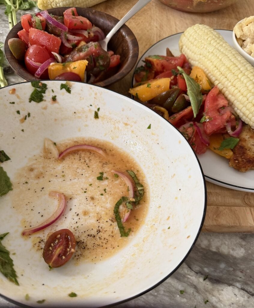 A white bowl with a little tomato drssing left in front of a bowl of Italian tomato salad and a plate of marinated tomatoes and corn.