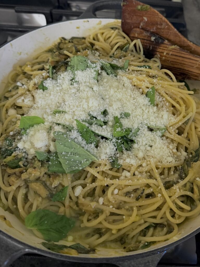 Cheese and basil and butter just added to zucchini spaghetti off the heat with wooden spoon in pan,
