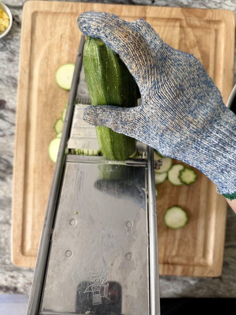 Using the mandoline to slice the zucchini into thin pieces.