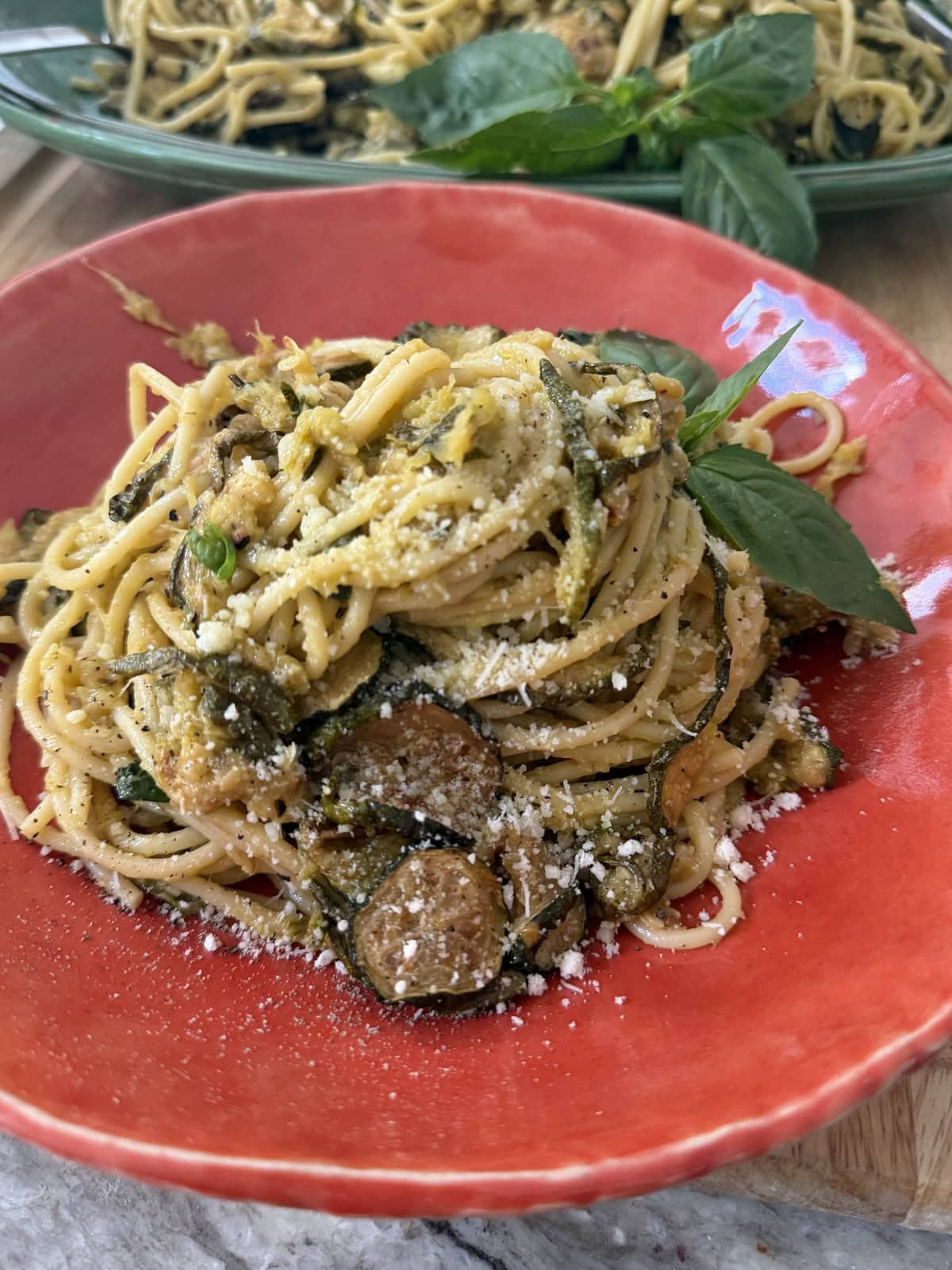 Spaghetti alla Nerano in orange pasta bowl with basil garnish.
