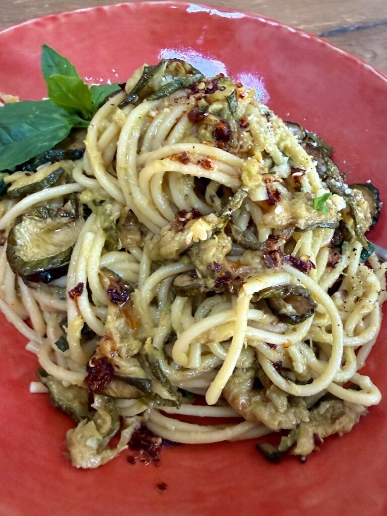 Pasta alla Nerano in orange pasta bowl with basil garnish and spicy oil.