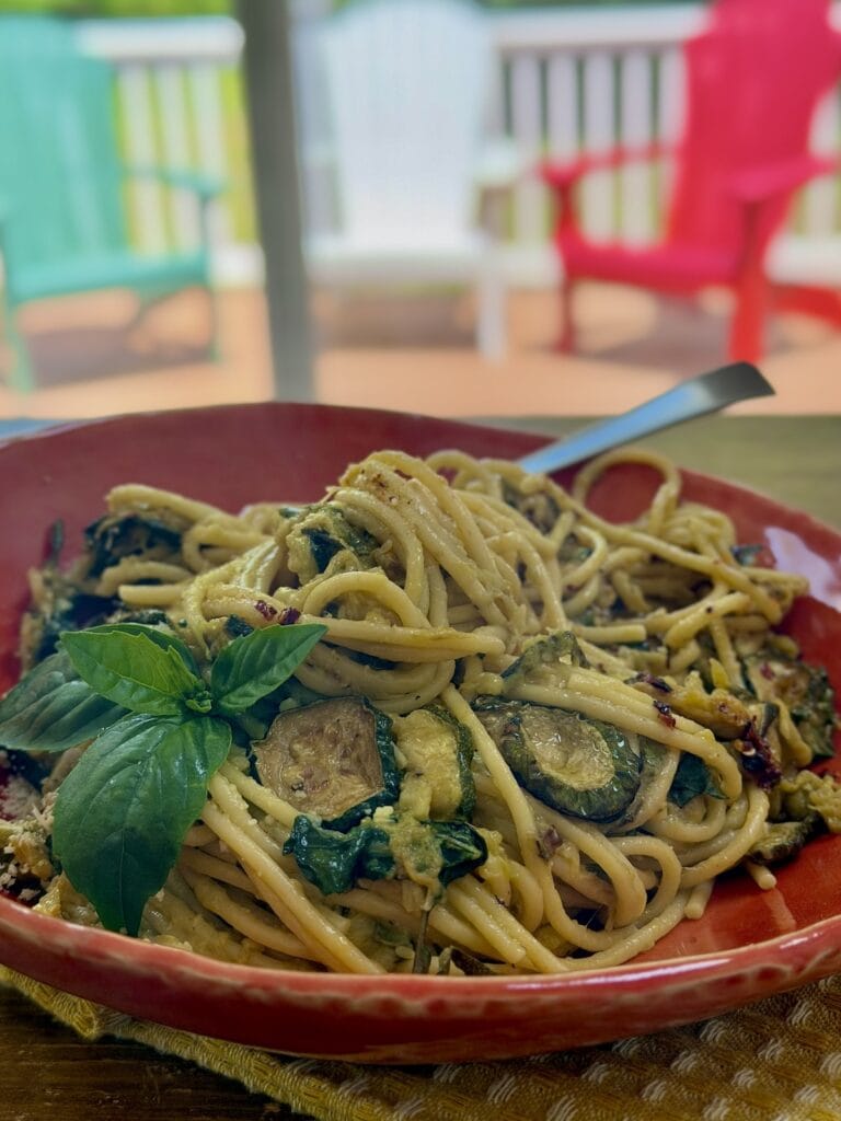 Zucchini Spaghetti in orange pasta bowl with basil garnish and fork, with deck chairs in the background